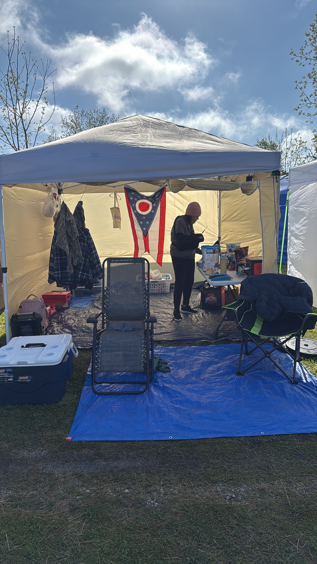 The crew basecamp tent at a backyard ultra, an Ohio flag hanging inside with a stocked supply table, coolers, and chairs ready between loops