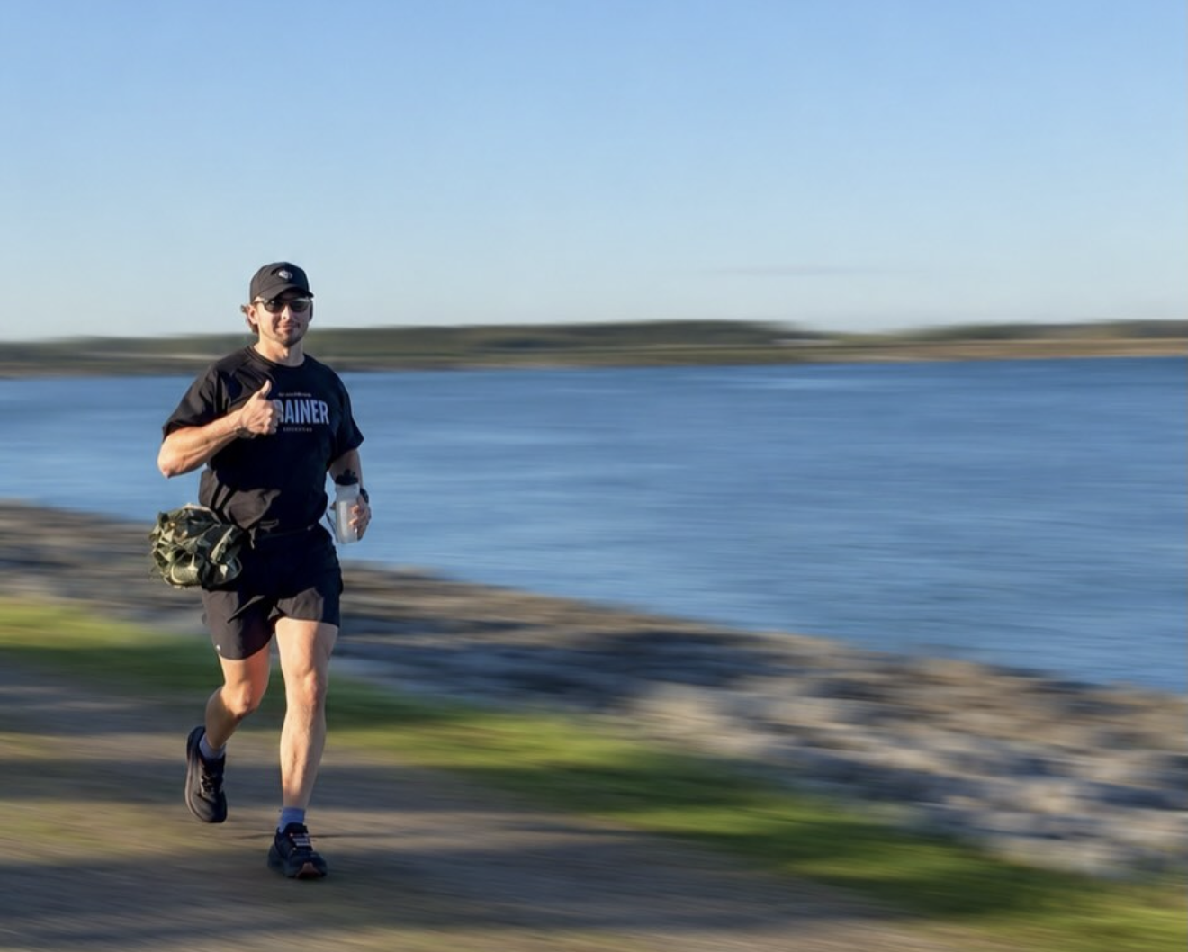 Adam Hettel giving a thumbs-up while running along a shoreline path at his last backyard ultra